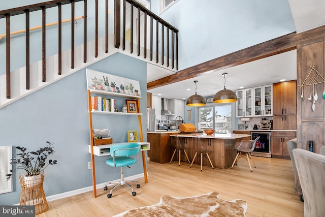 kitchen featuring wine cooler, wall chimney range hood, light hardwood / wood-style floors, a breakfast bar, and hanging light fixtures