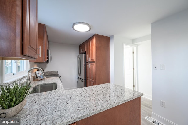 kitchen with sink, light wood-type flooring, light stone countertops, kitchen peninsula, and stainless steel refrigerator