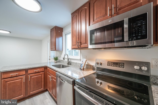 kitchen featuring light stone countertops, appliances with stainless steel finishes, kitchen peninsula, sink, and light hardwood / wood-style flooring