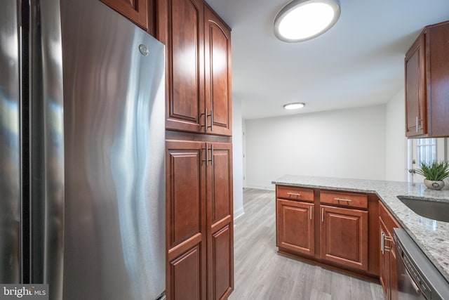 kitchen featuring sink, light stone counters, stainless steel appliances, and light hardwood / wood-style flooring