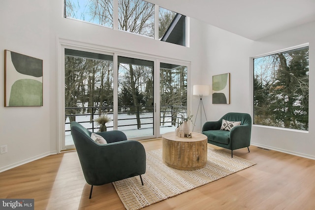 living area featuring plenty of natural light, light wood-type flooring, and a towering ceiling