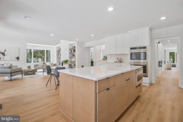 kitchen with stainless steel double oven, a kitchen island, decorative backsplash, white cabinets, and light wood-type flooring