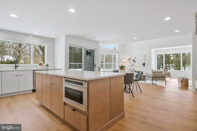 kitchen with light hardwood / wood-style floors, a center island, white cabinetry, and sink