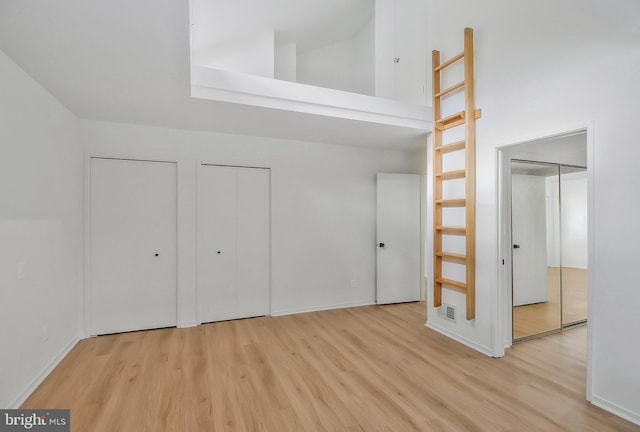 unfurnished bedroom with a towering ceiling, light wood-type flooring, and multiple closets