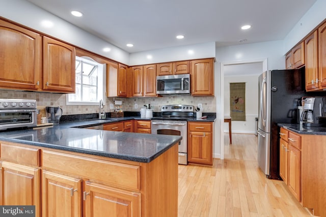 kitchen featuring appliances with stainless steel finishes, sink, backsplash, kitchen peninsula, and light hardwood / wood-style flooring