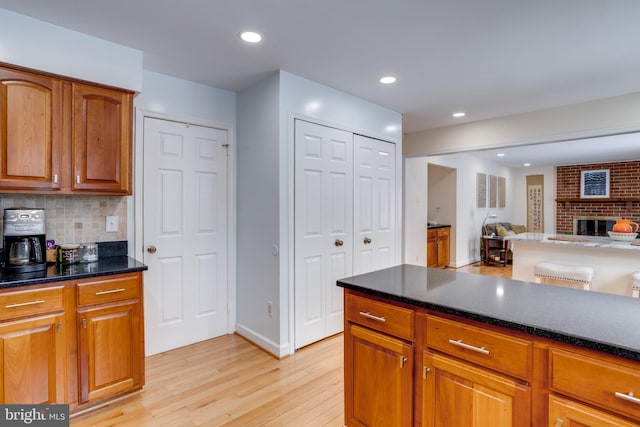 kitchen featuring a brick fireplace, backsplash, light hardwood / wood-style flooring, and dark stone counters