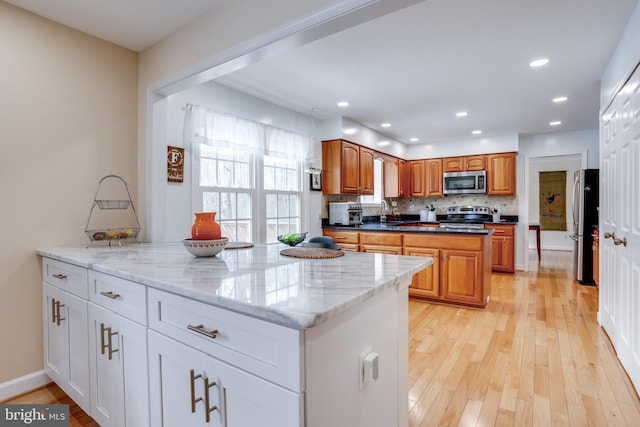 kitchen with light hardwood / wood-style floors, white cabinetry, light stone countertops, and appliances with stainless steel finishes