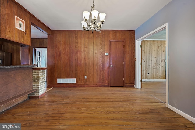 unfurnished dining area featuring hardwood / wood-style floors, a notable chandelier, wood walls, and a fireplace