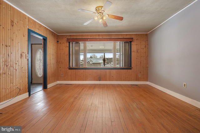 unfurnished room with hardwood / wood-style flooring, ceiling fan, crown molding, and wooden walls