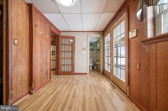 entryway featuring light wood-type flooring, french doors, a paneled ceiling, and wood walls