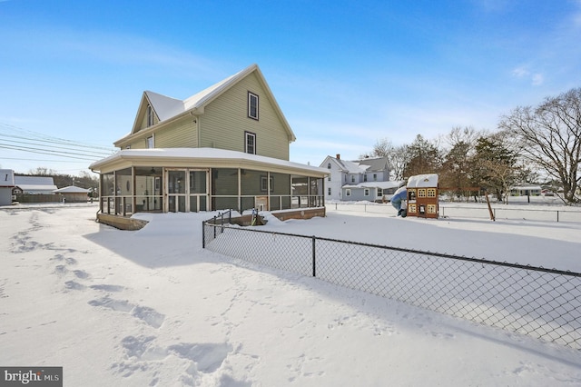 snow covered rear of property with a sunroom