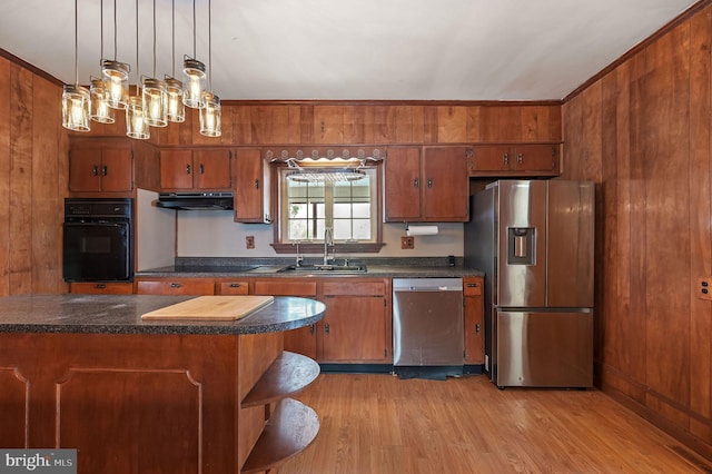 kitchen featuring light wood-type flooring, stainless steel appliances, wooden walls, sink, and decorative light fixtures