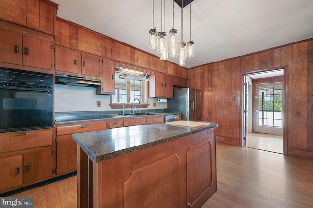 kitchen with sink, wood walls, black appliances, a kitchen island, and exhaust hood