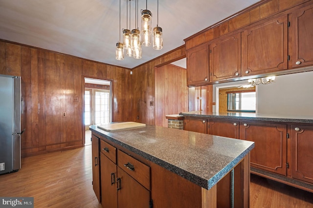 kitchen with stainless steel fridge, wooden walls, pendant lighting, an inviting chandelier, and a center island