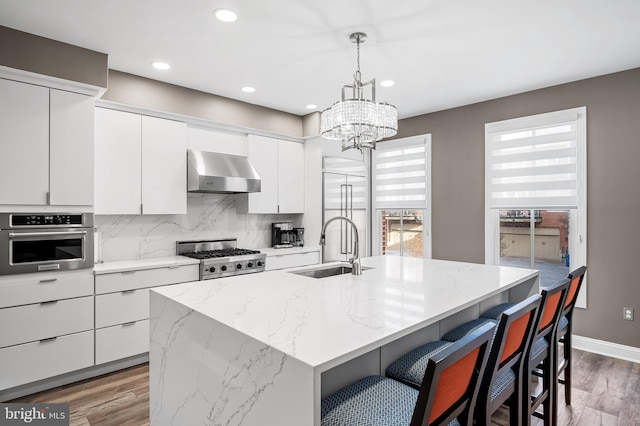 kitchen with appliances with stainless steel finishes, decorative light fixtures, a kitchen island with sink, and exhaust hood