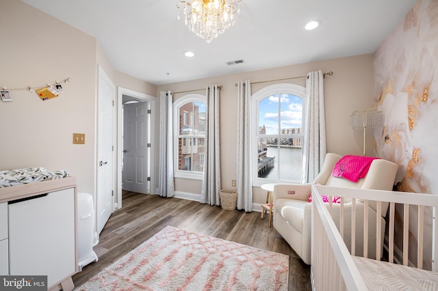 bedroom with hardwood / wood-style floors, a chandelier, and a nursery area