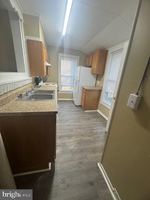 kitchen with white refrigerator, light wood-type flooring, lofted ceiling, and sink