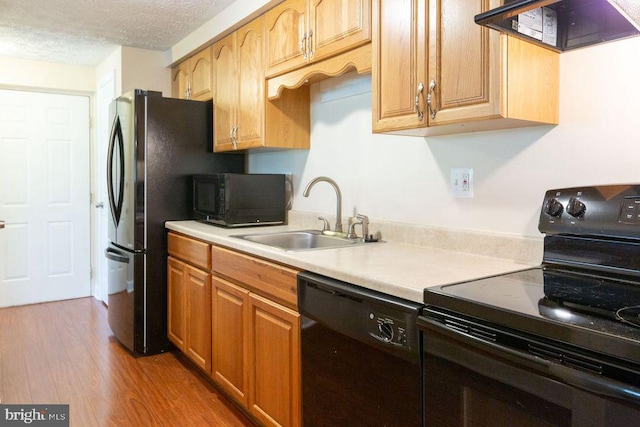 kitchen with sink, ventilation hood, a textured ceiling, black appliances, and light wood-type flooring