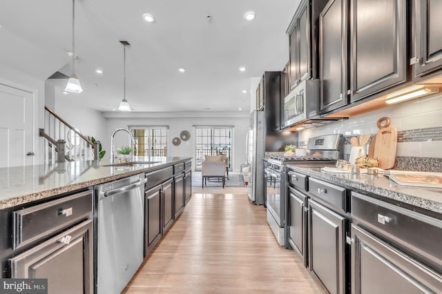 kitchen with light hardwood / wood-style floors, light stone countertops, sink, pendant lighting, and stainless steel appliances