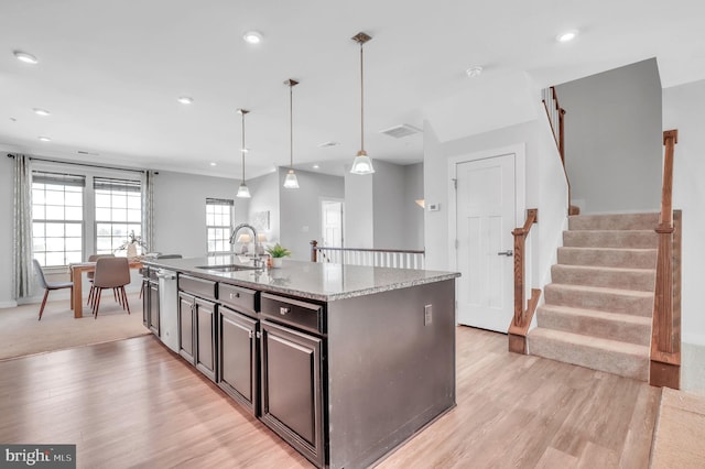 kitchen with pendant lighting, an island with sink, sink, light wood-type flooring, and light stone counters