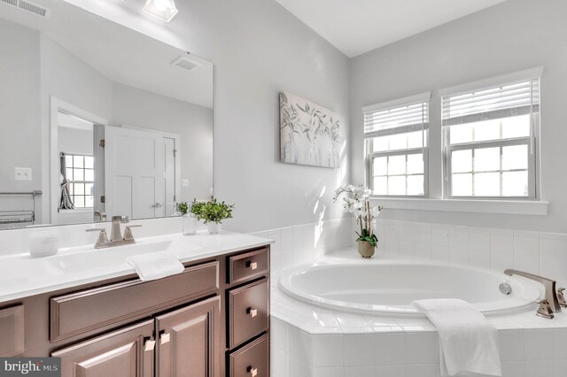 bathroom featuring tiled tub, a wealth of natural light, and vanity