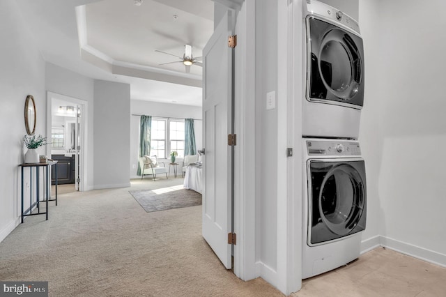 laundry area with ceiling fan, stacked washer / dryer, and light carpet