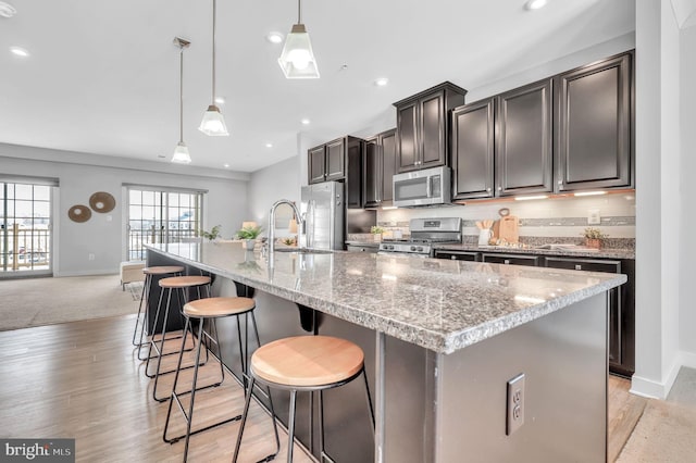 kitchen featuring a kitchen breakfast bar, pendant lighting, stainless steel appliances, and an island with sink