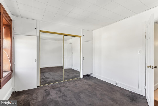 unfurnished bedroom with dark colored carpet and a closet