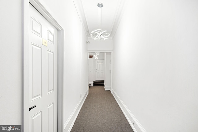 corridor with a notable chandelier, dark carpet, crown molding, and baseboards