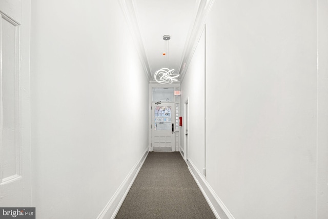 corridor featuring ornamental molding, baseboards, and dark colored carpet