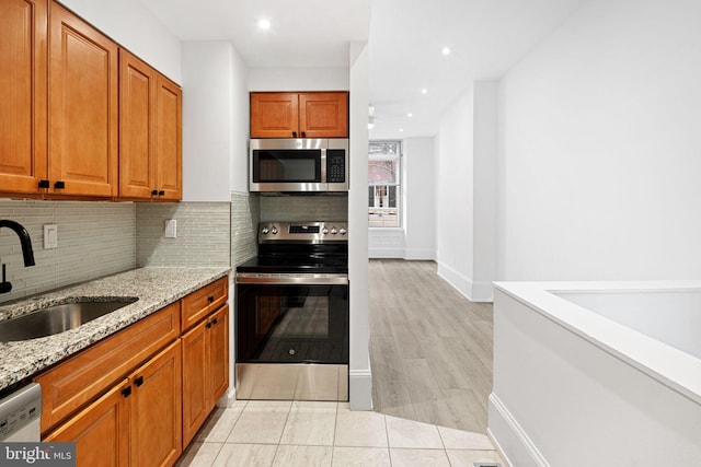 kitchen with tasteful backsplash, light stone counters, brown cabinets, appliances with stainless steel finishes, and a sink