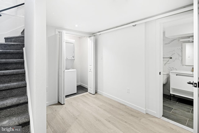 unfurnished bedroom featuring baseboards, light wood-style floors, ensuite bath, and stacked washer / dryer