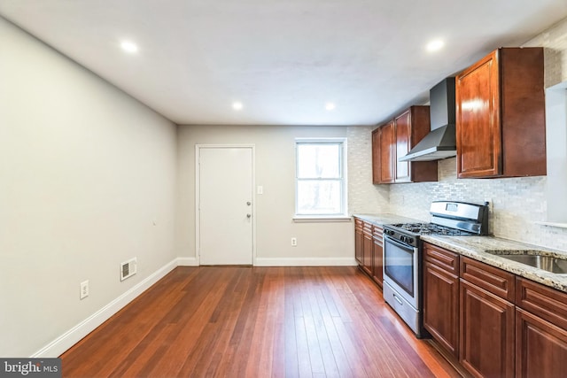 kitchen with tasteful backsplash, dark hardwood / wood-style flooring, stainless steel gas stove, wall chimney exhaust hood, and light stone counters