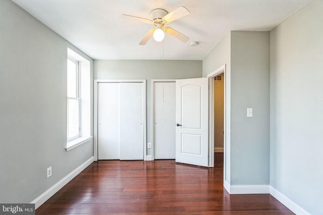 unfurnished bedroom featuring ceiling fan, two closets, and dark hardwood / wood-style floors