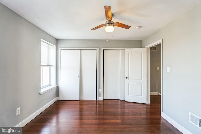 unfurnished bedroom with ceiling fan, multiple windows, dark hardwood / wood-style flooring, and multiple closets