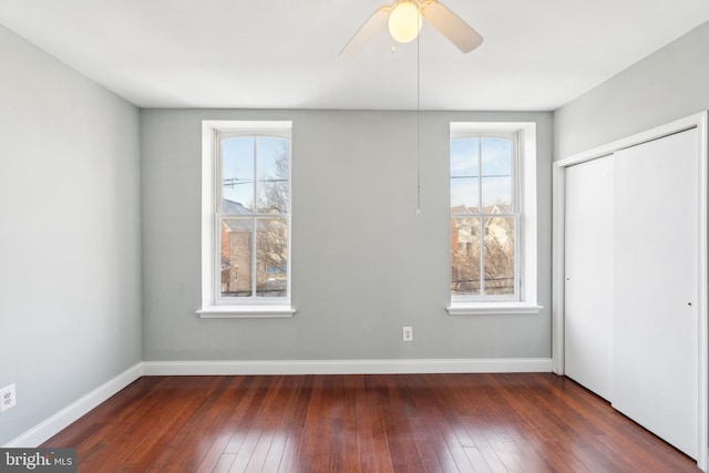 unfurnished bedroom with ceiling fan, dark hardwood / wood-style flooring, a closet, and multiple windows