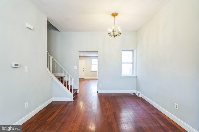 empty room with dark wood-type flooring and a notable chandelier