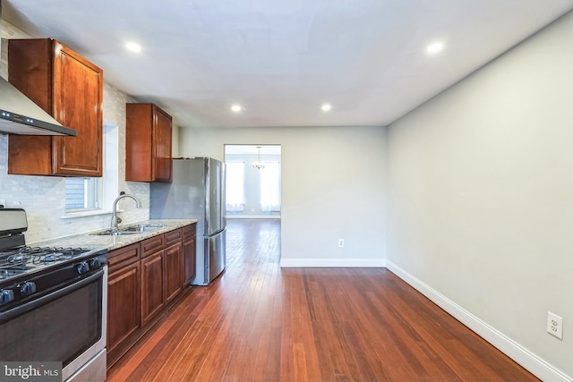 kitchen with wall chimney range hood, sink, dark wood-type flooring, appliances with stainless steel finishes, and light stone counters