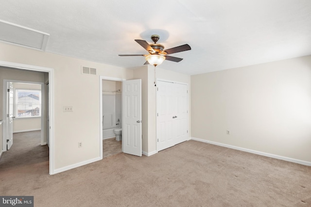 unfurnished bedroom with a closet, light colored carpet, ceiling fan, and connected bathroom