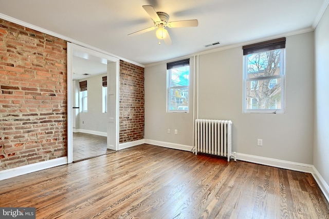 unfurnished room with radiator, ceiling fan, brick wall, hardwood / wood-style flooring, and ornamental molding