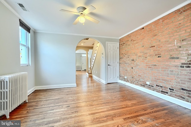 spare room featuring radiator, crown molding, ceiling fan, wood-type flooring, and brick wall