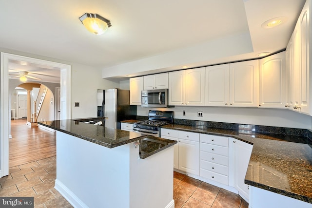 kitchen with stainless steel appliances, ceiling fan, dark stone countertops, white cabinets, and a kitchen island