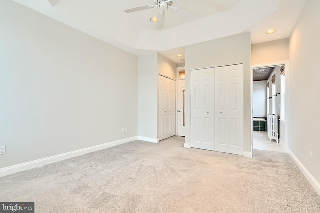 unfurnished bedroom featuring light colored carpet, ceiling fan, and multiple closets