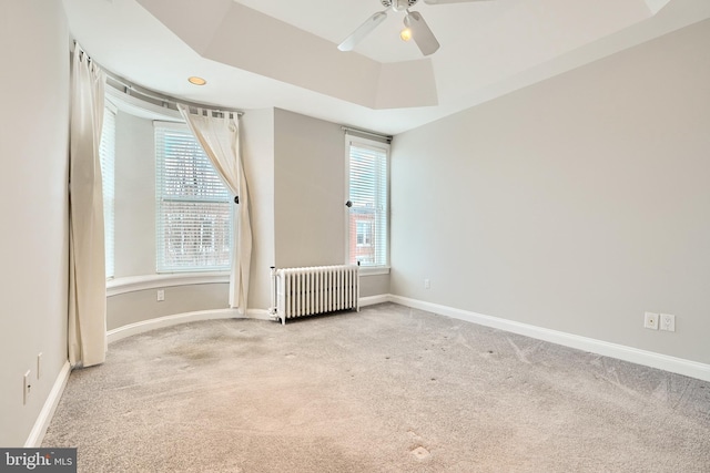 empty room featuring a wealth of natural light, light colored carpet, radiator, and a tray ceiling