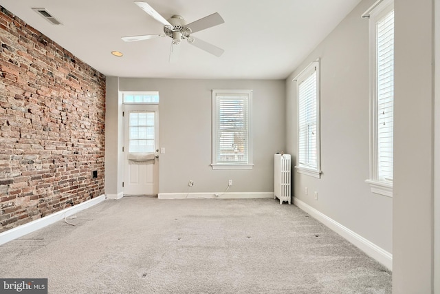 carpeted spare room with ceiling fan, radiator heating unit, and brick wall