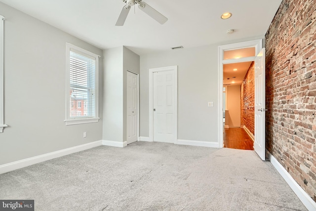 unfurnished bedroom with light carpet, a closet, ceiling fan, and brick wall