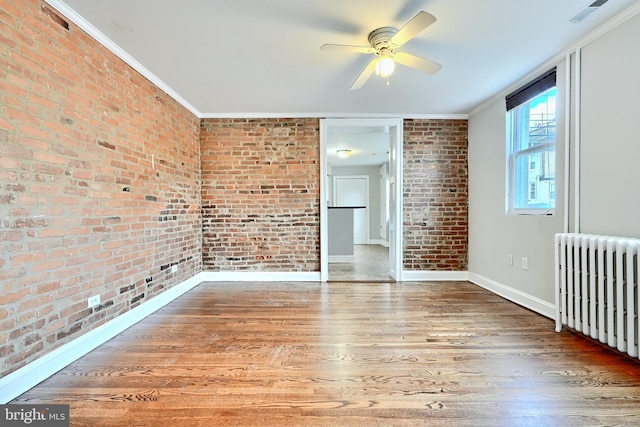 interior space featuring ceiling fan, radiator heating unit, brick wall, hardwood / wood-style floors, and ornamental molding