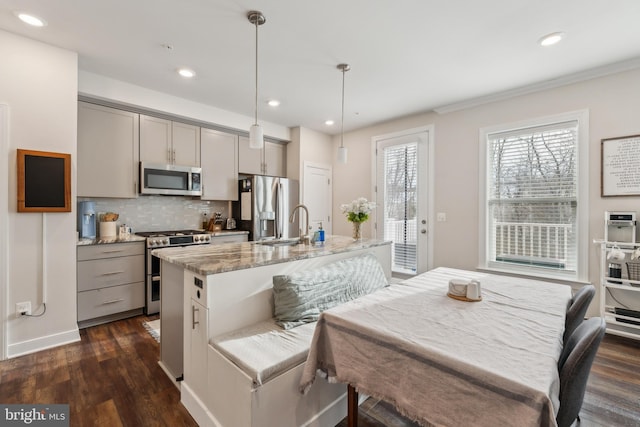 kitchen with pendant lighting, stainless steel appliances, an island with sink, dark hardwood / wood-style floors, and gray cabinetry