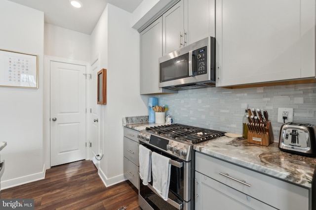 kitchen with light stone countertops, appliances with stainless steel finishes, gray cabinetry, decorative backsplash, and dark wood-type flooring