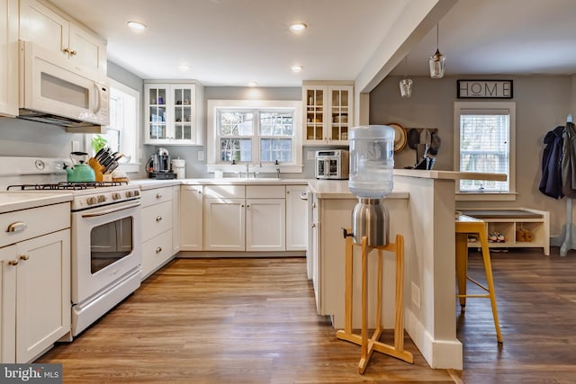 kitchen with light hardwood / wood-style flooring, pendant lighting, white appliances, a breakfast bar, and white cabinets